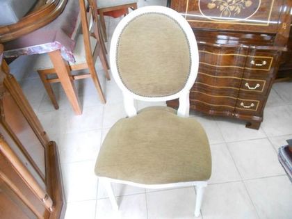 Silla tapizada en blanco con asiento beige y respaldo ovalado sobre un suelo de baldosas, junto a muebles de madera.