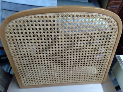 Respaldo de silla de ratán con estructura de madera y parte superior curvada, visto de cerca.