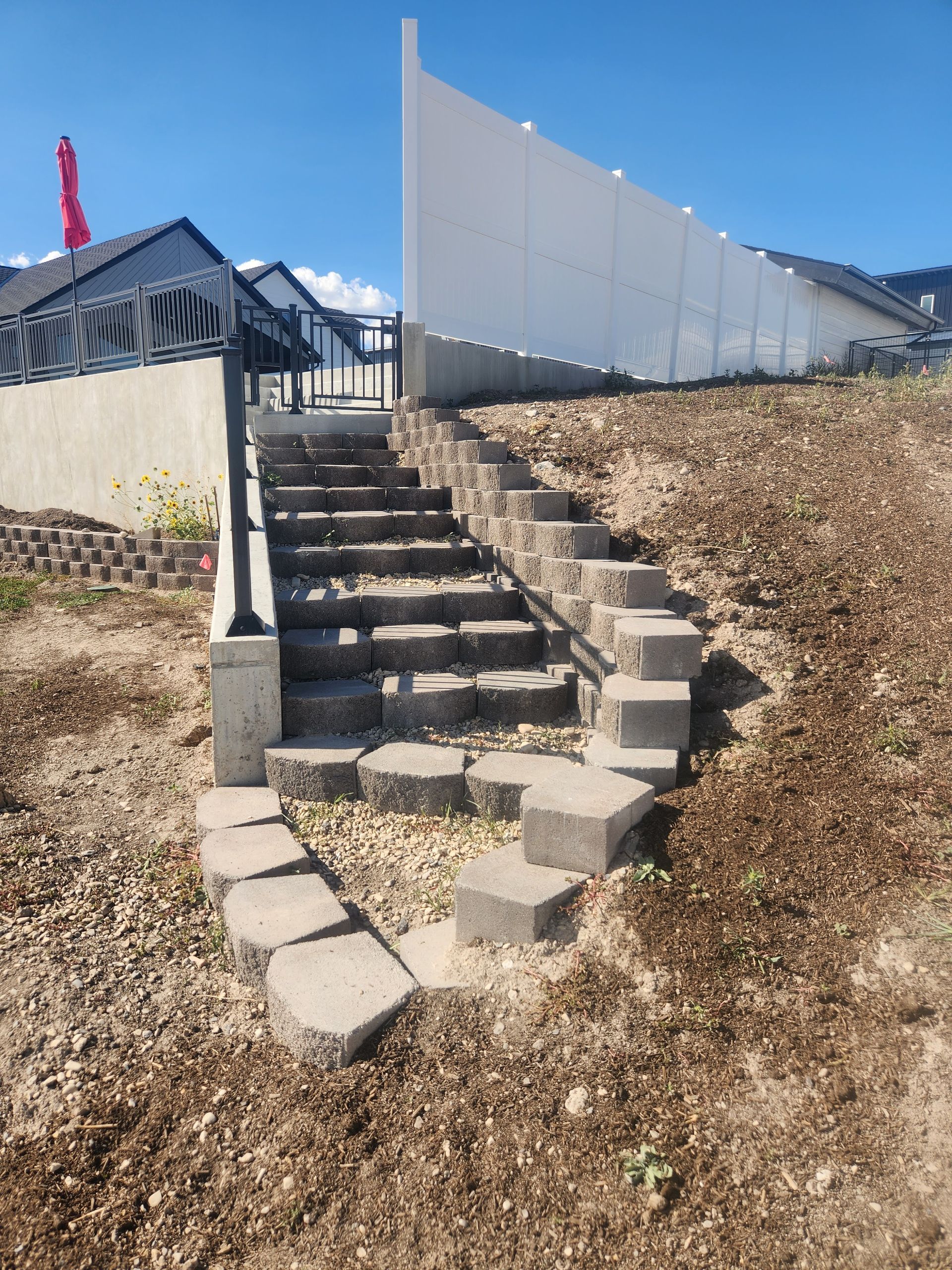 Stone steps leading up a hillside to a fence and gate, under a clear blue sky.