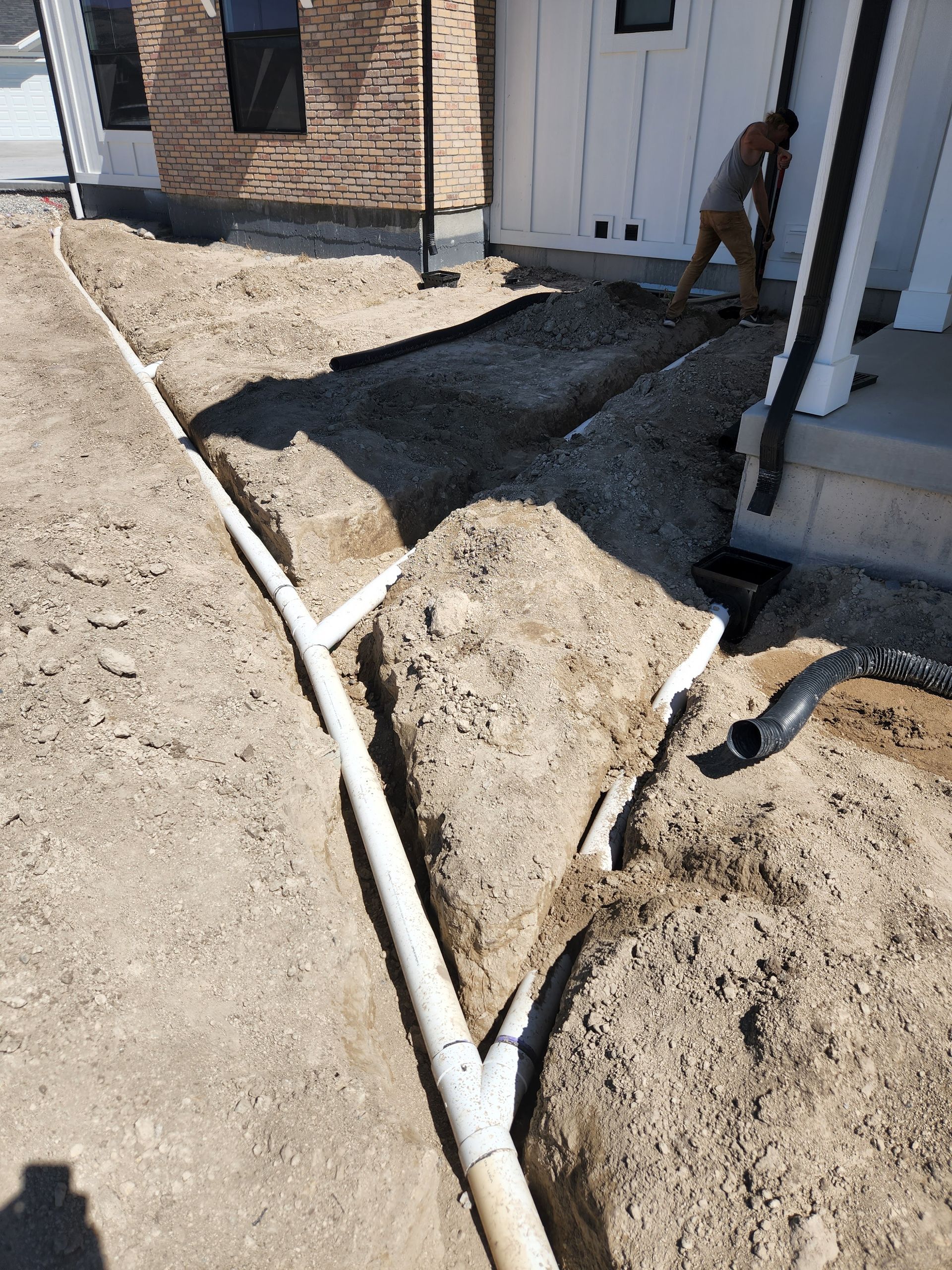 Drainage pipes being installed at a construction site near a house, with a worker.