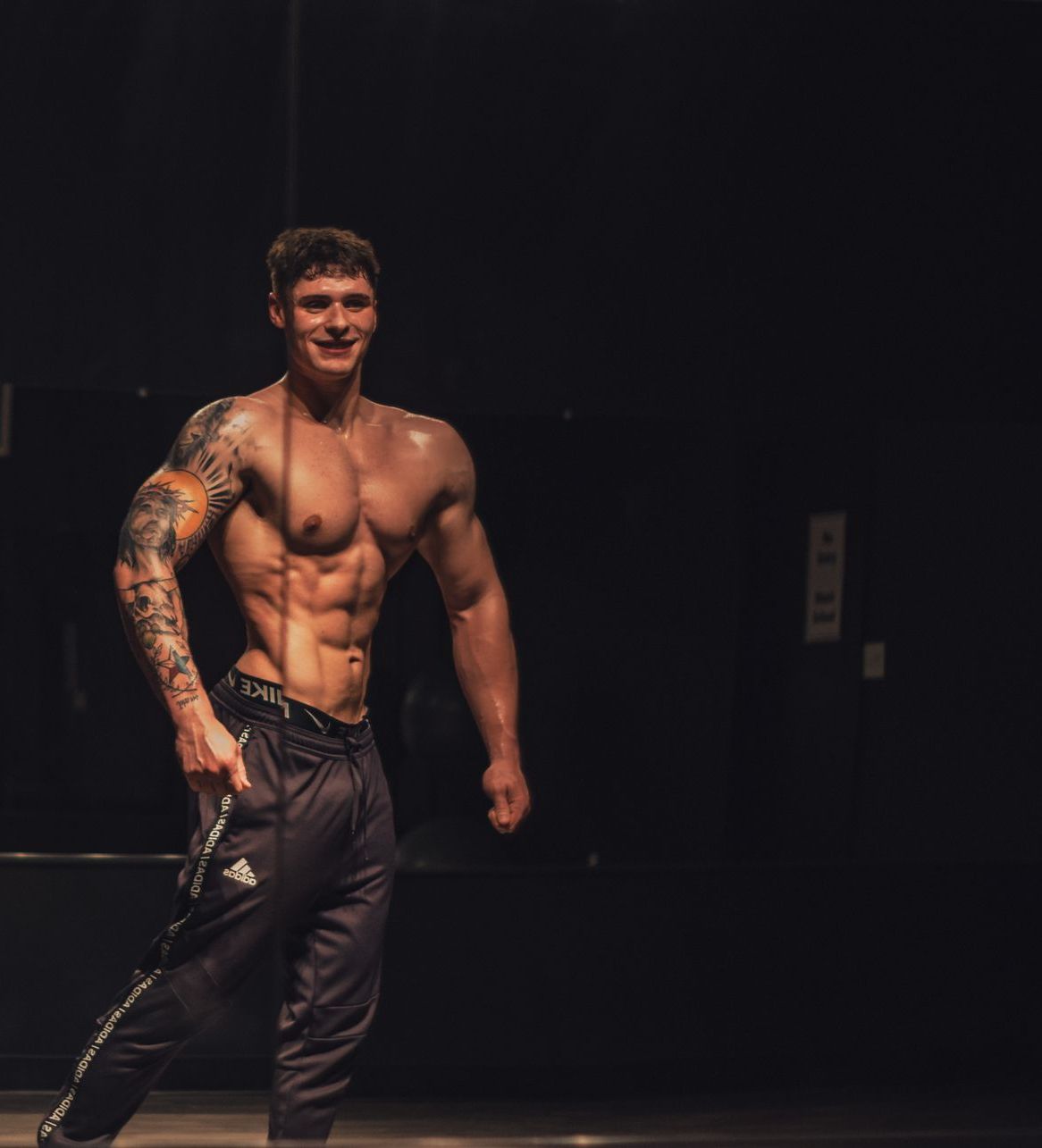 A shirtless man with a tattoo on his arm is standing in a dark room