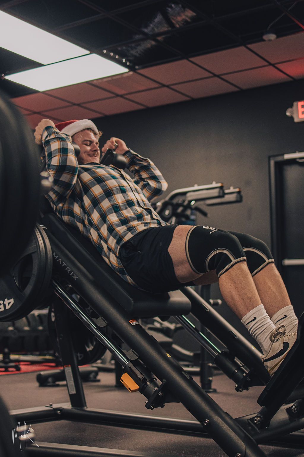 A man wearing a santa hat is sitting on a machine in a gym.
