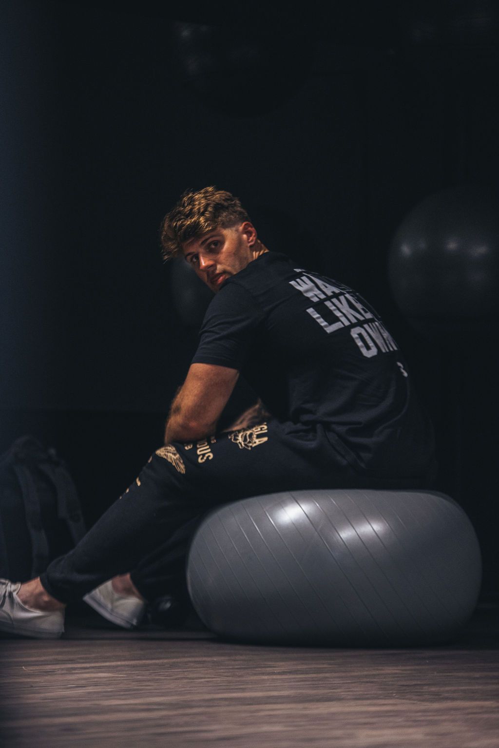 A man is sitting on an exercise ball in a dark room.