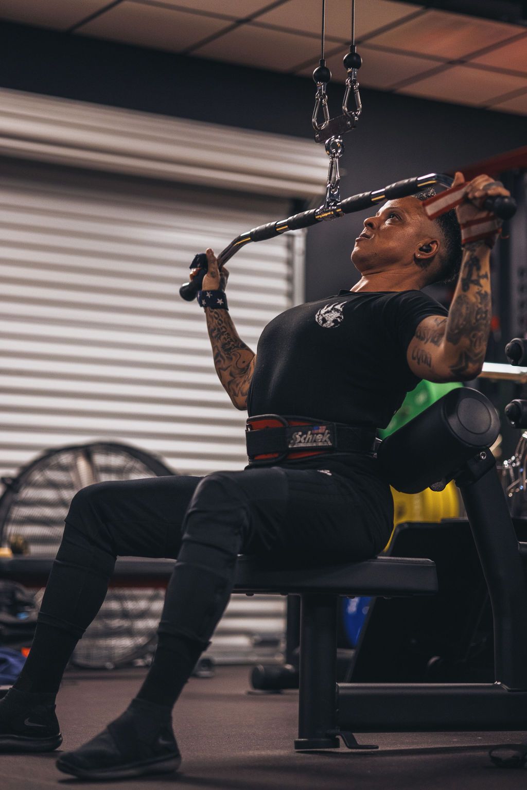 A man is sitting on a bench in a gym using a lat pulldown machine.