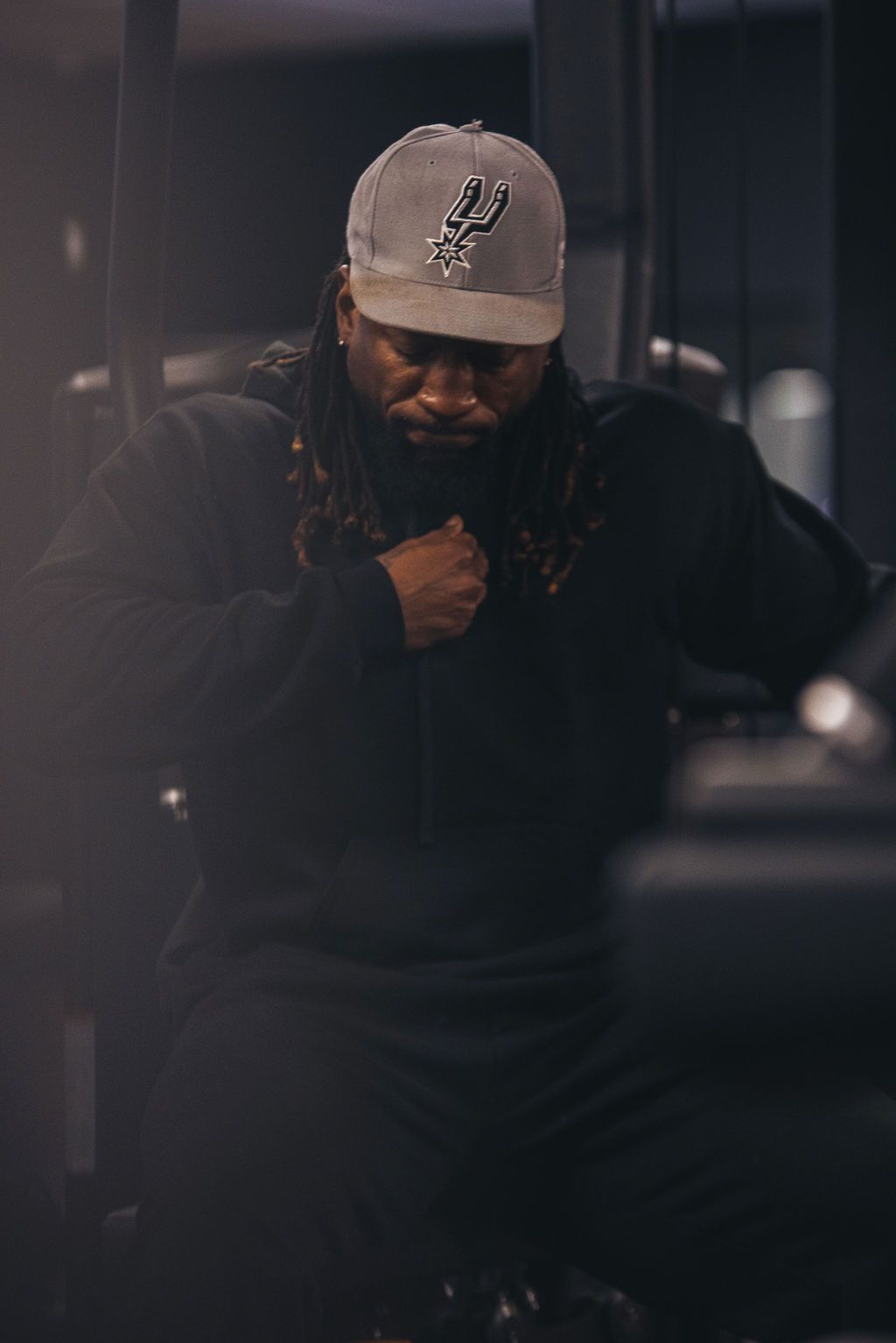 A man wearing a hat and a black hoodie is standing in a dark room.