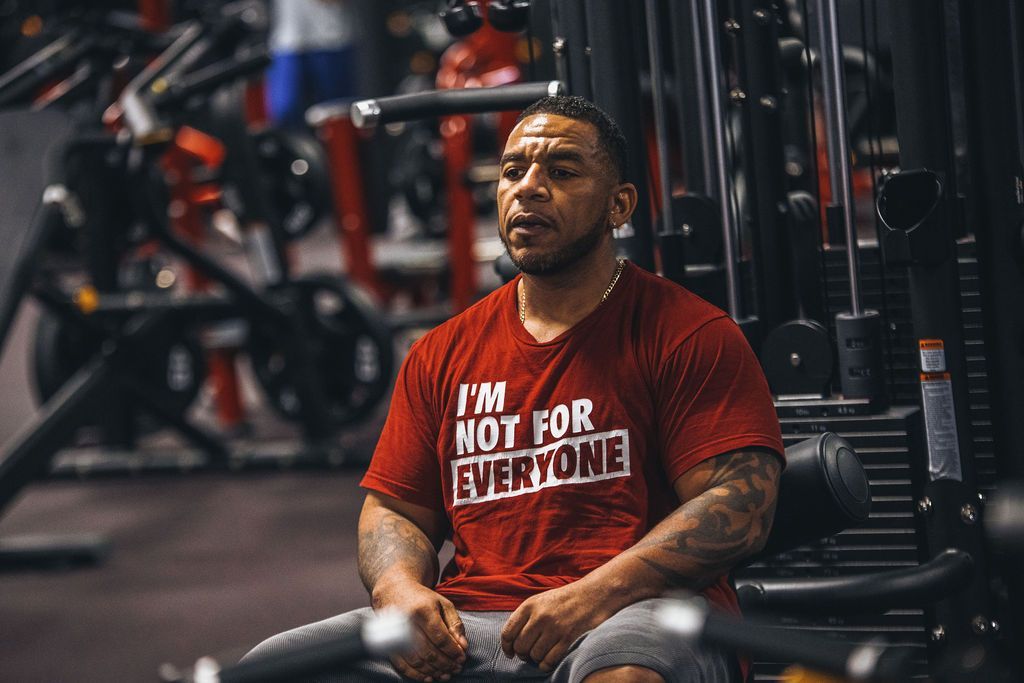 A man in a red shirt is sitting on a machine in a gym.