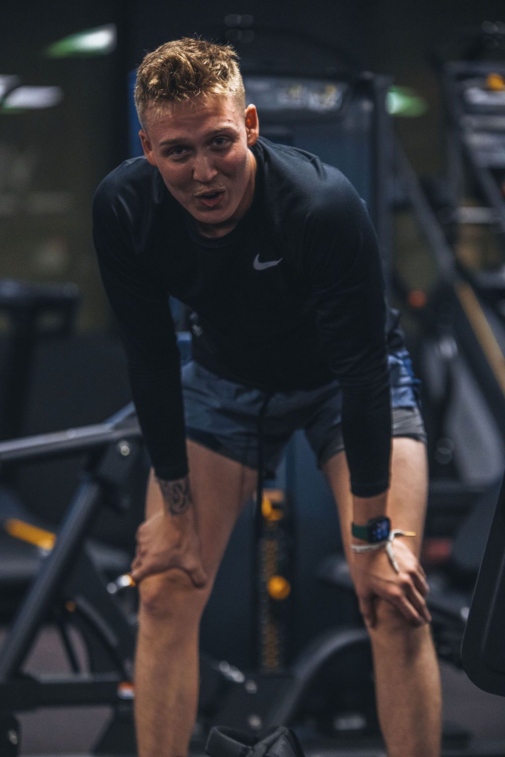 A man is standing in a gym with his hands on his knees.
