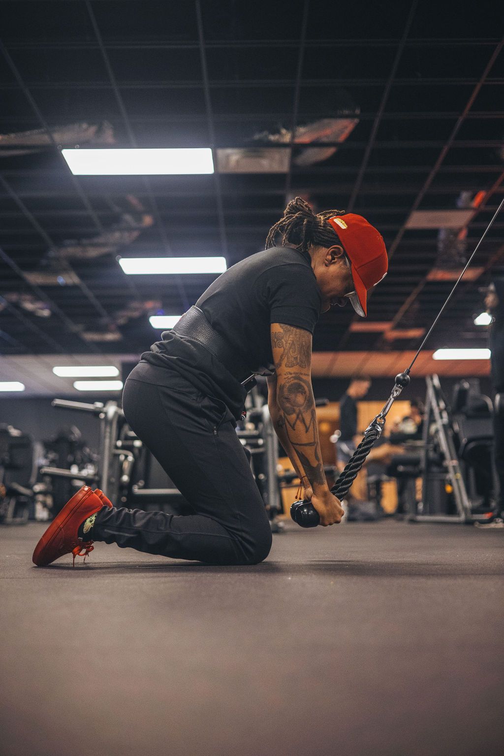 A man is kneeling down in a gym while using a machine.