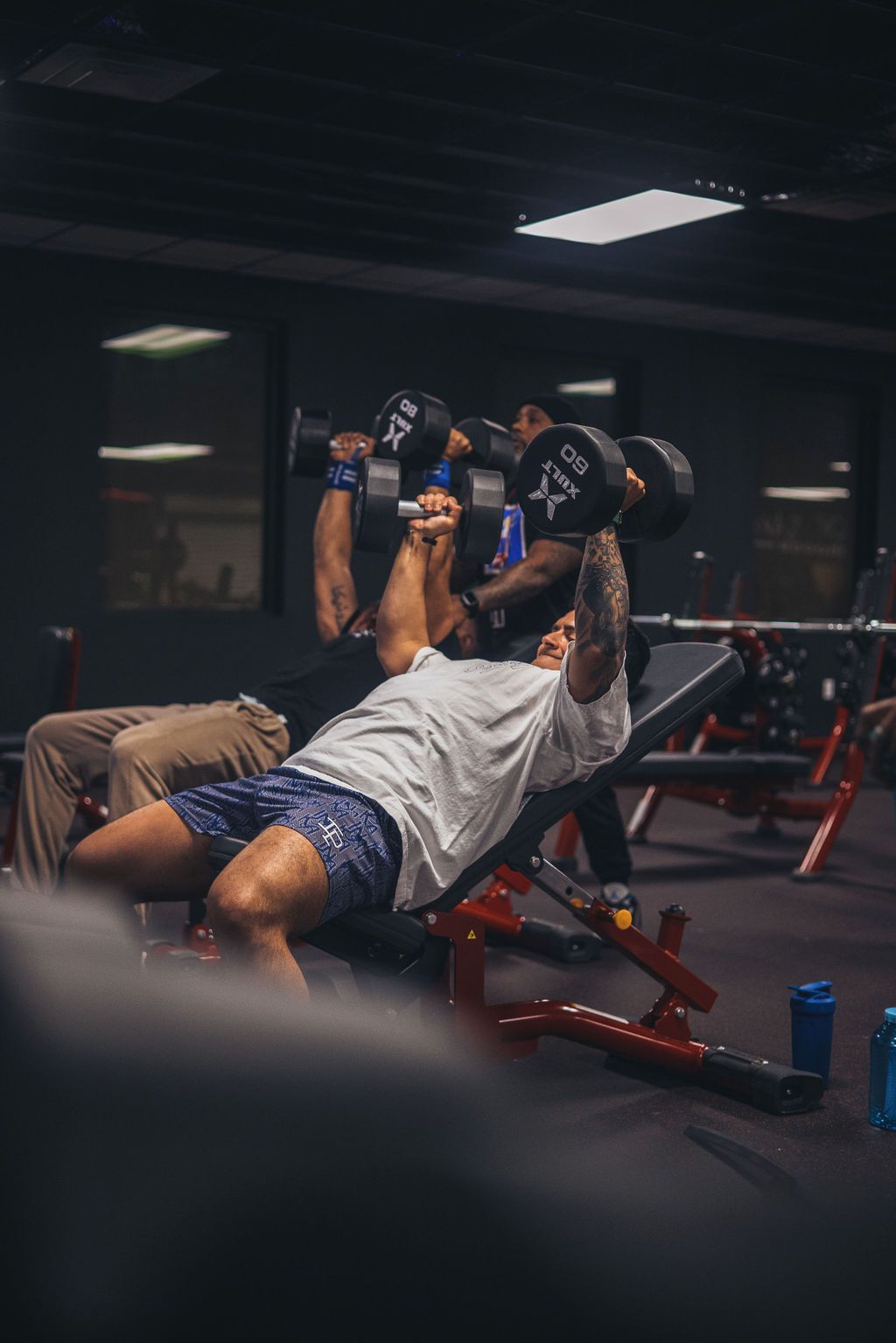 A man is lifting dumbbells on a bench in a gym.