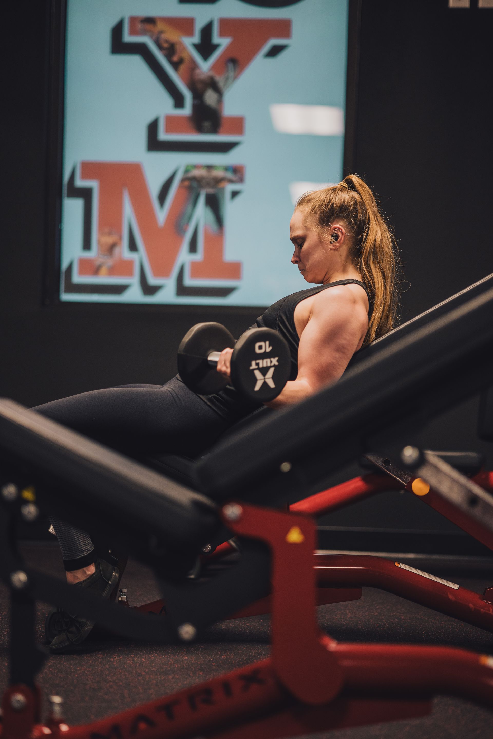 A woman is sitting on a bench in a gym holding a dumbbell.