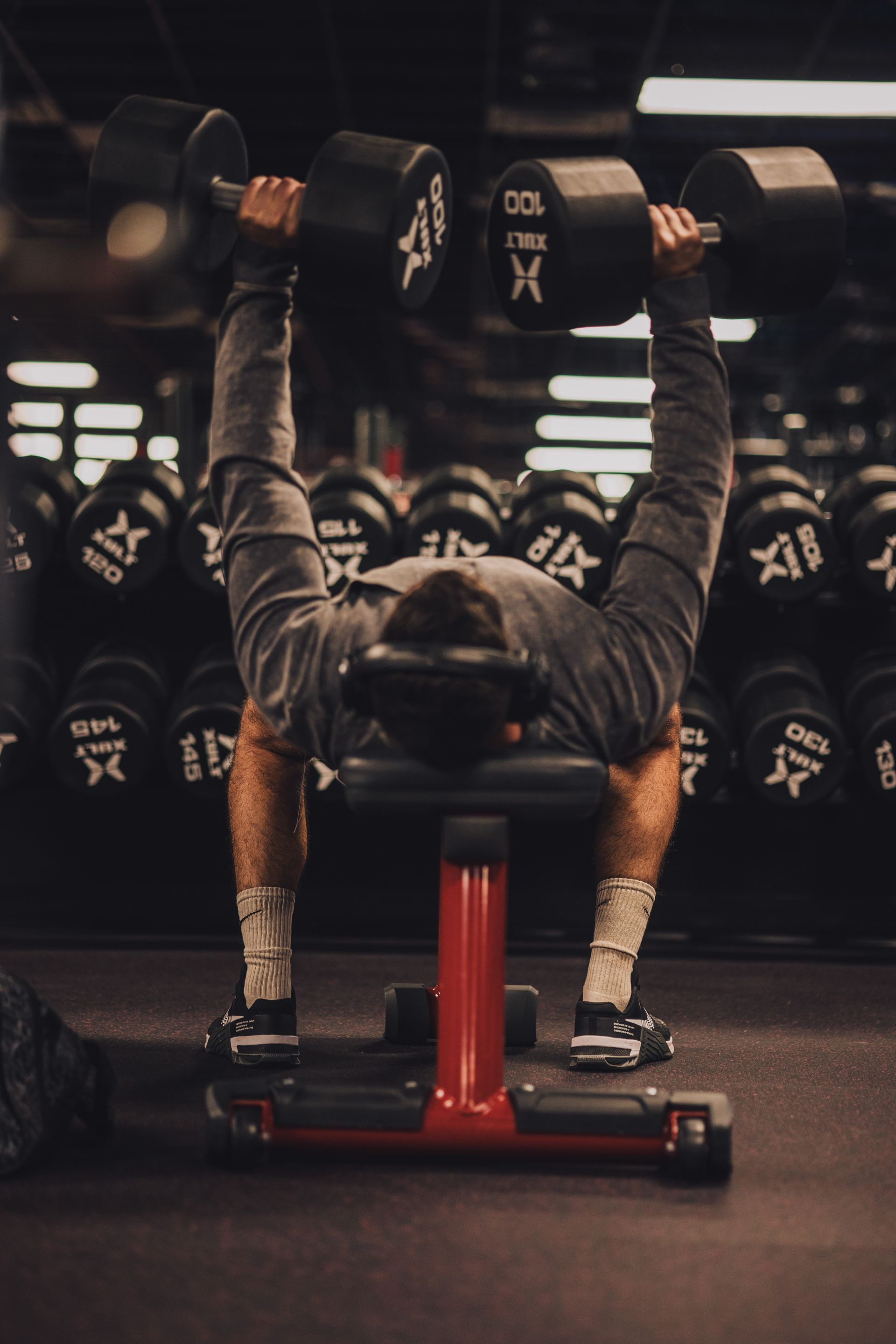 A man is lifting dumbbells on a bench in a gym.