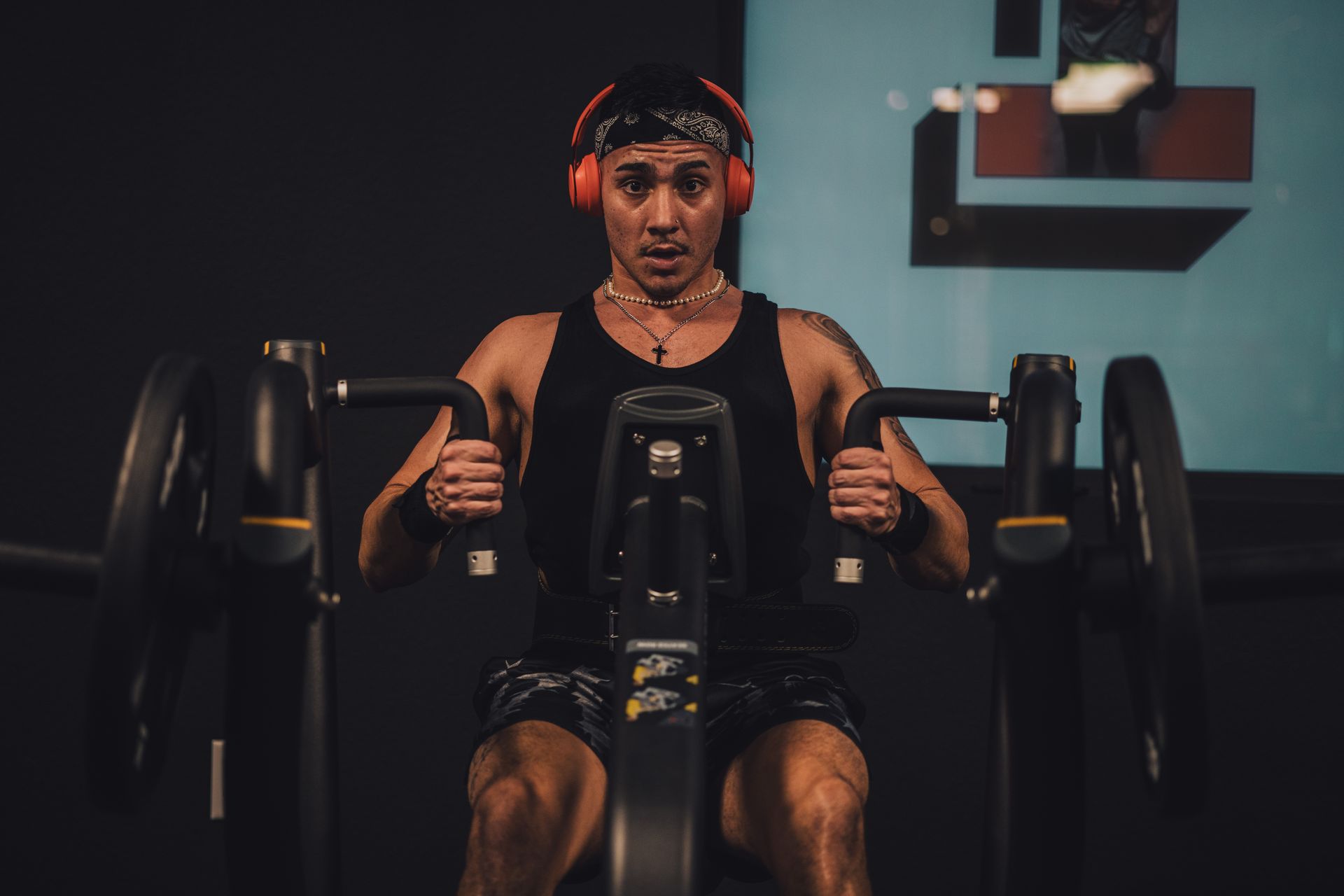 A man wearing headphones is riding an exercise bike in a gym.