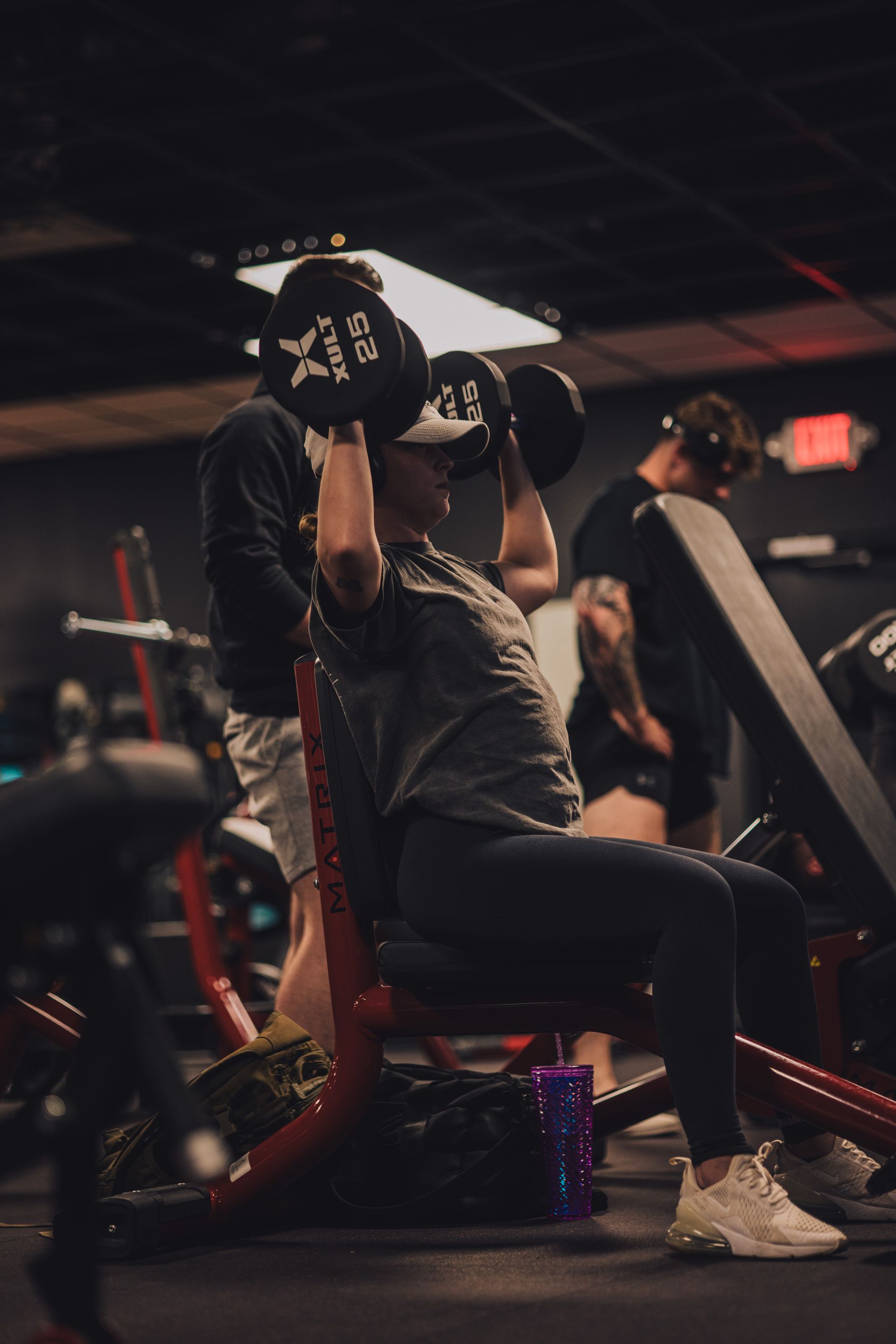 A man is lifting a dumbbell while sitting on a bench in a gym.