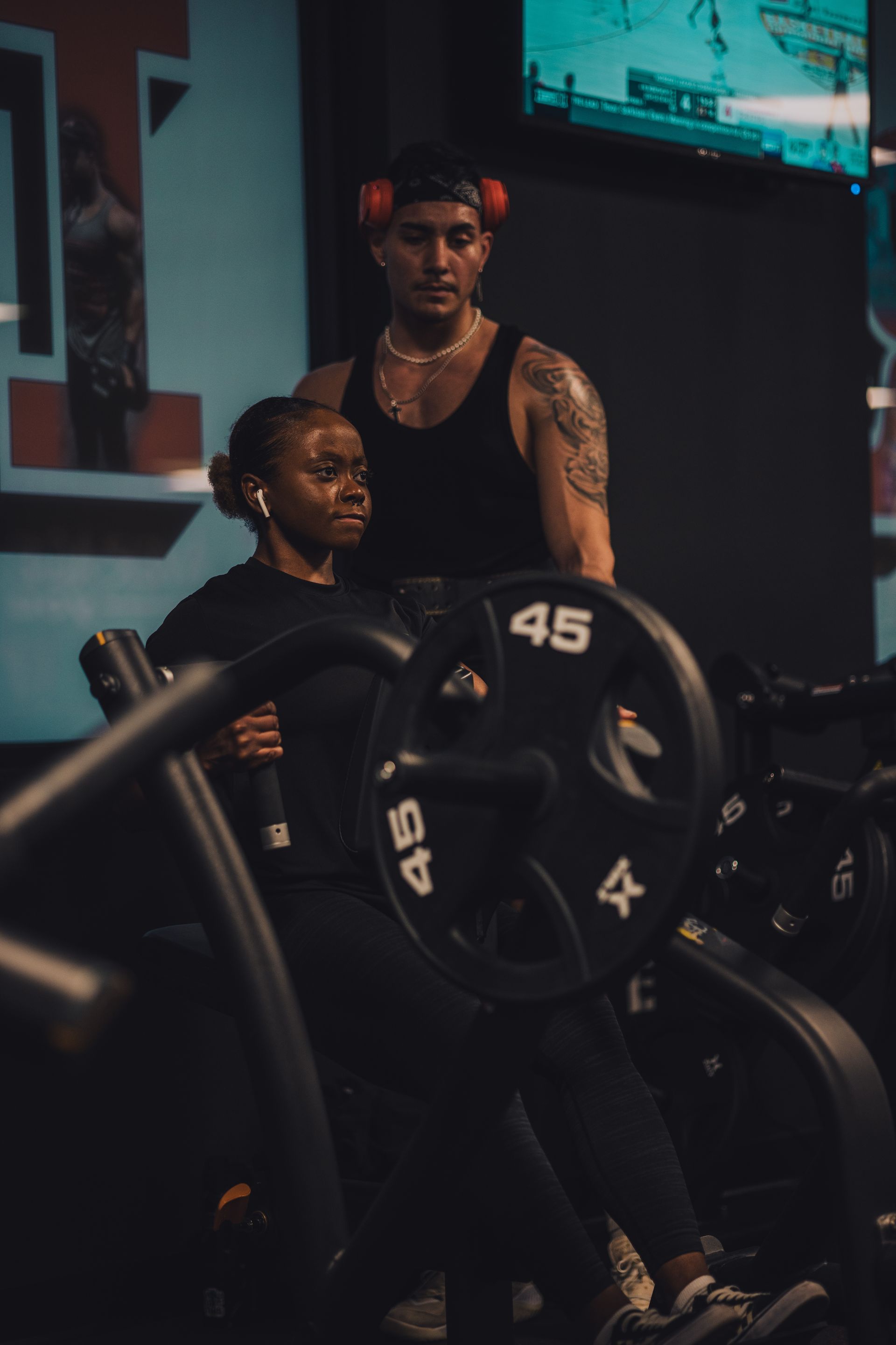 A man is standing next to a woman sitting on a machine in a gym.