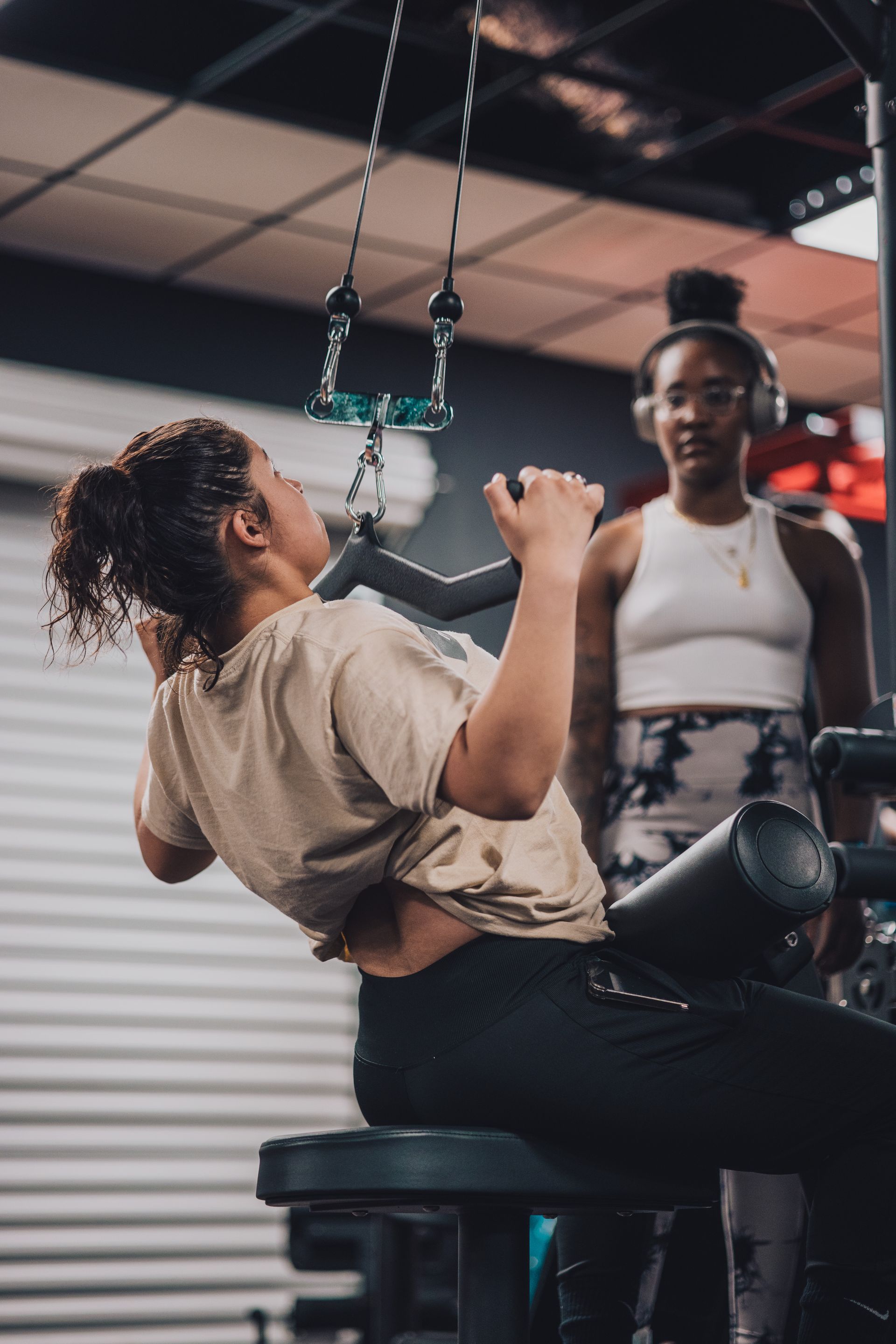 A woman is using a machine in a gym while another woman watches.