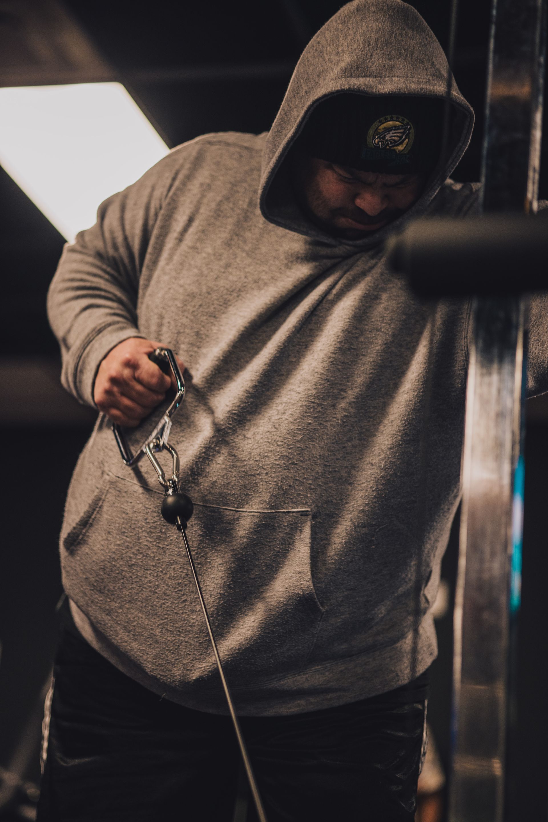 A man in a hoodie is using a machine in a gym.