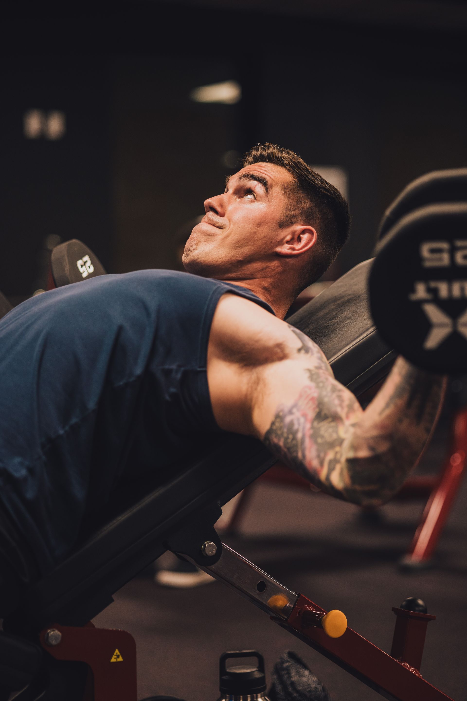 A man is lifting a barbell on a bench in a gym.