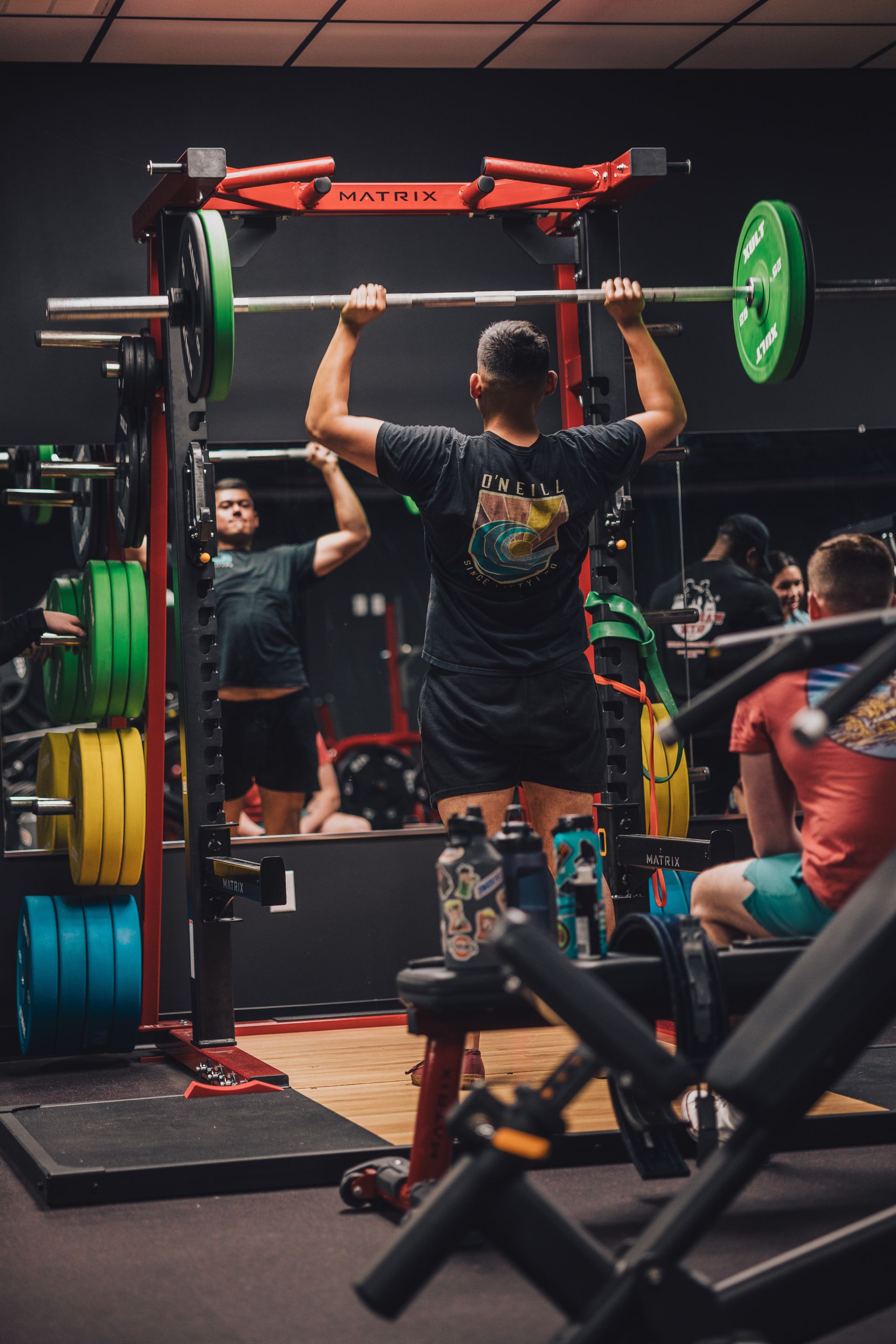 A man is lifting a barbell over his head in a gym.