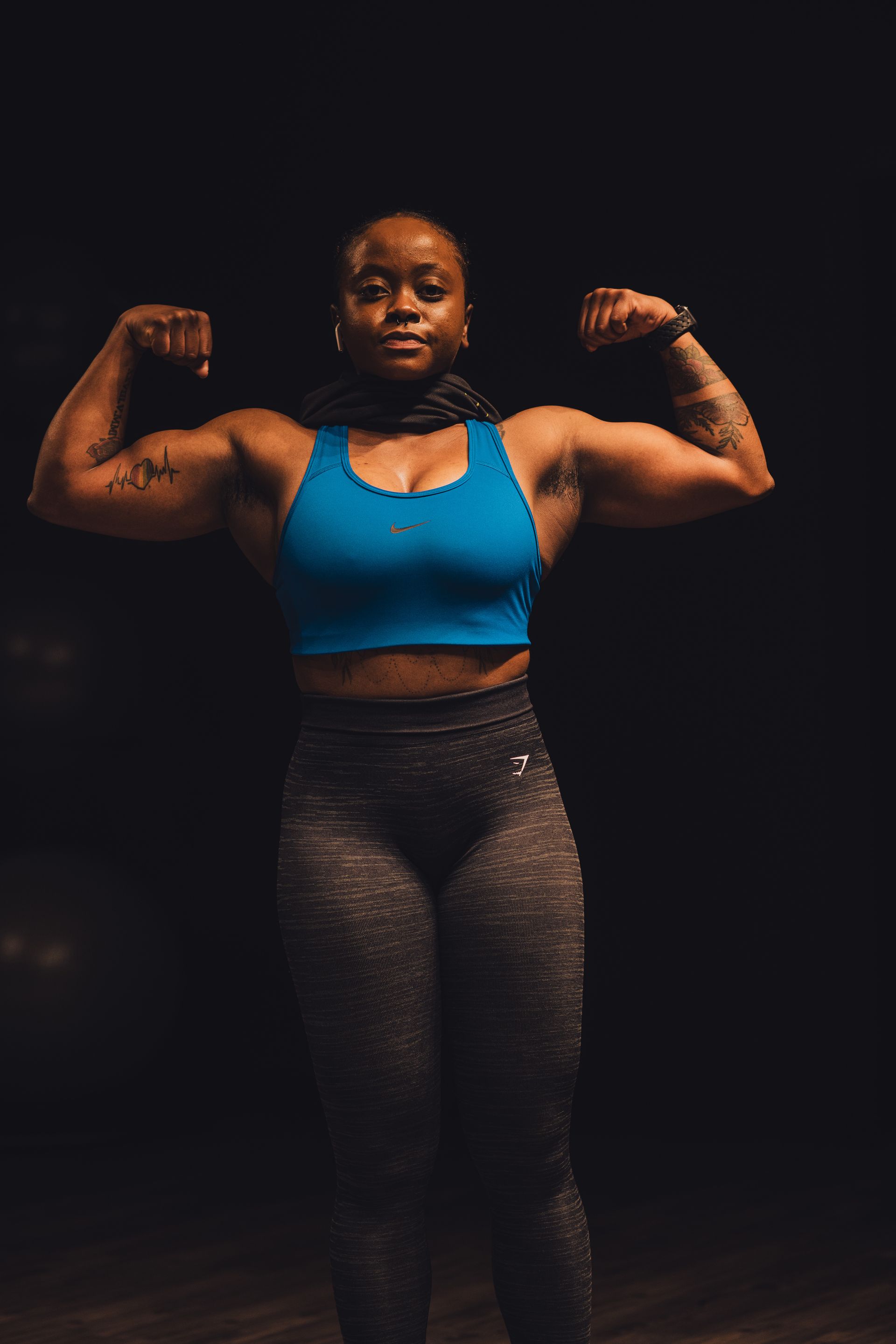 A woman is flexing her muscles in a dark room.