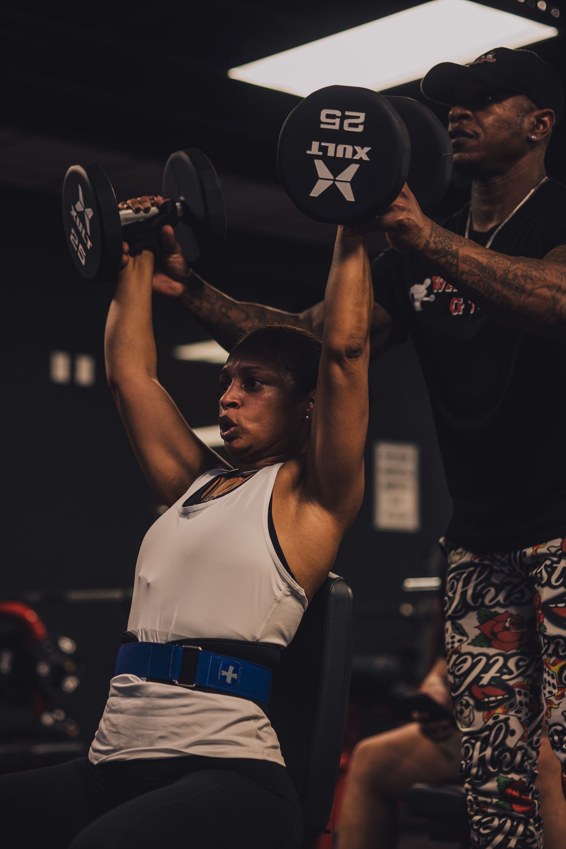 A woman is lifting a dumbbell over her head in a gym.