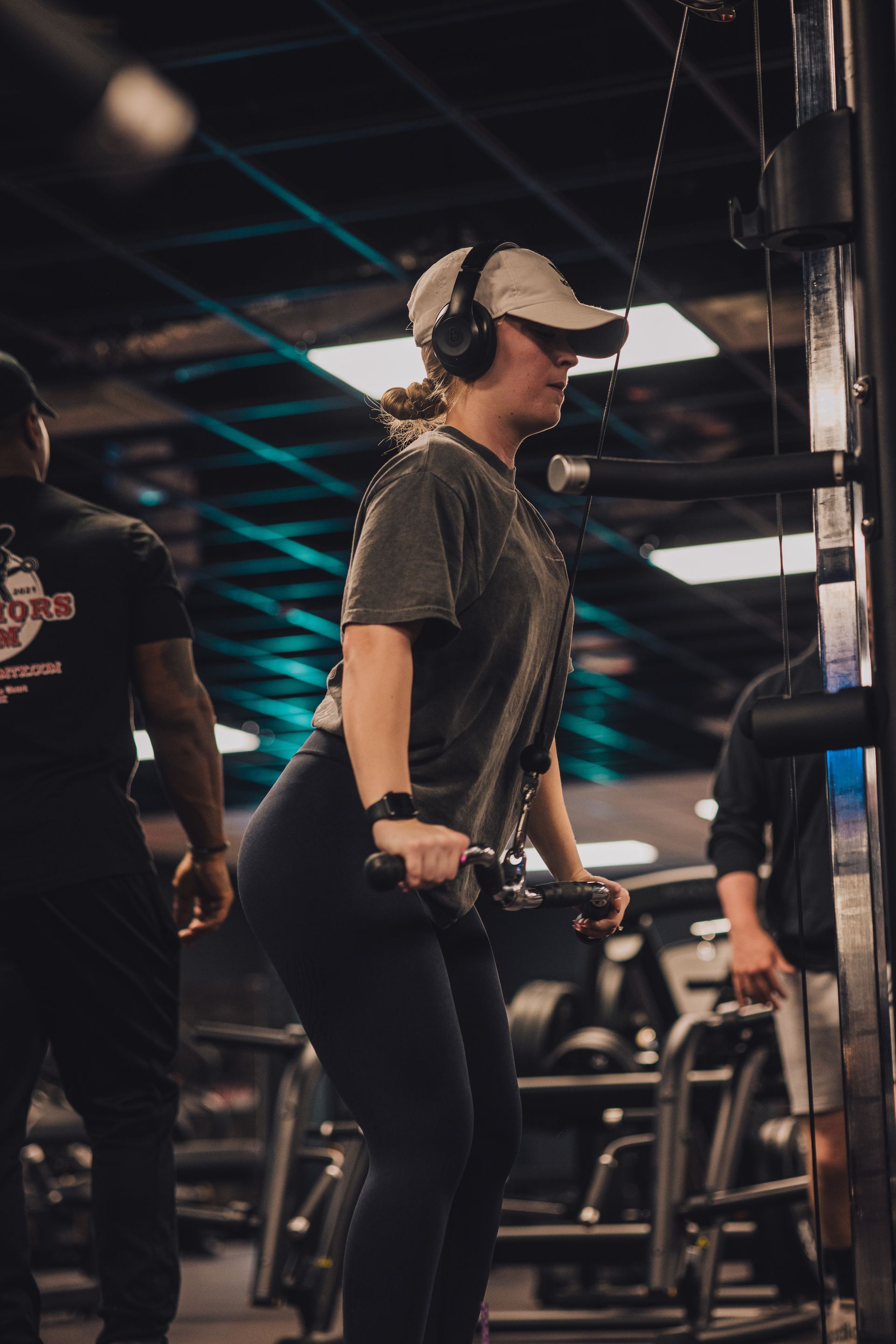 A woman is lifting a dumbbell in a gym while wearing headphones.