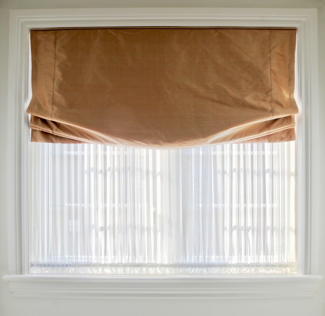 Una finestra con una tenda romana marrone e tende bianche.