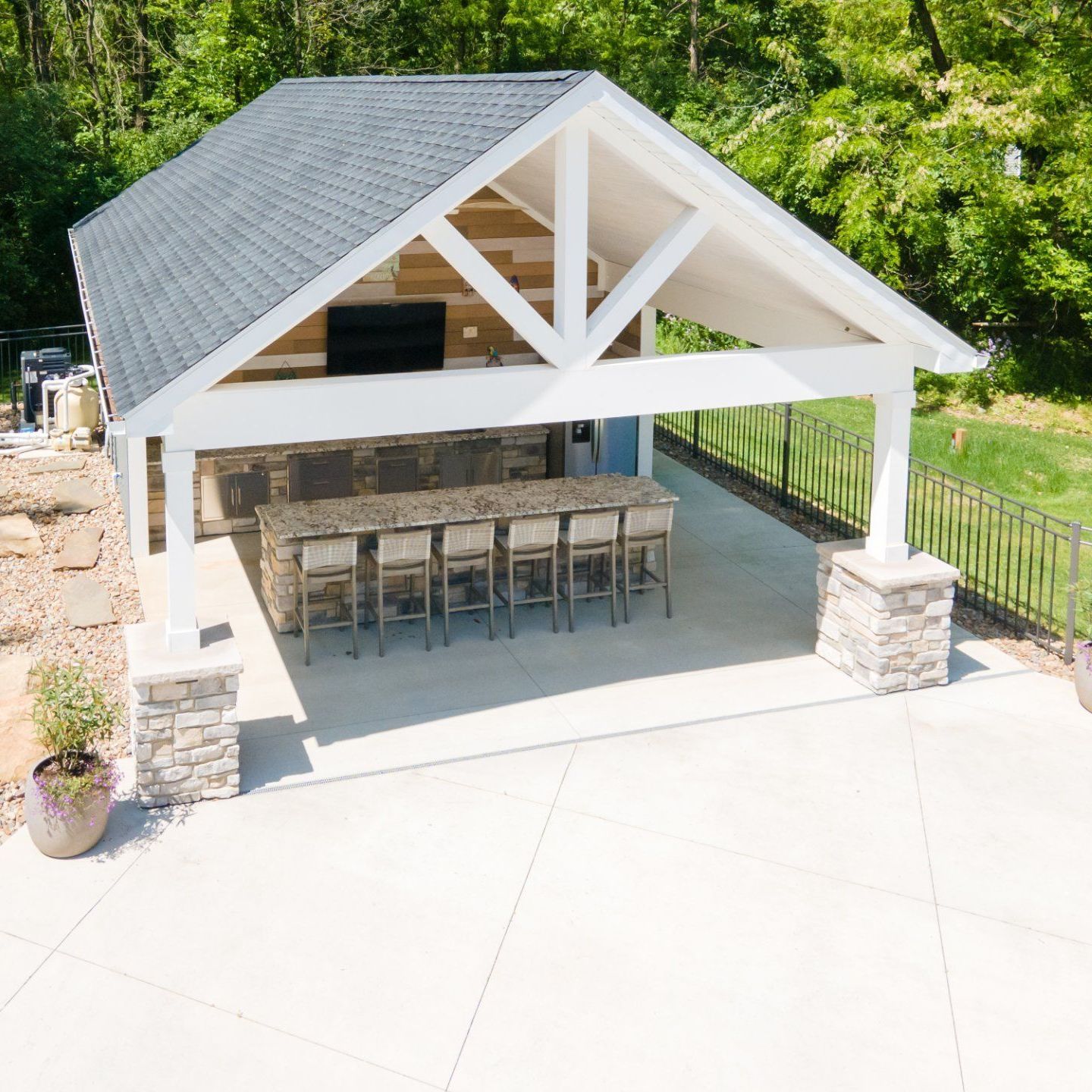 Outdoor kitchen with a bar, seating, and a TV under a gable roof.