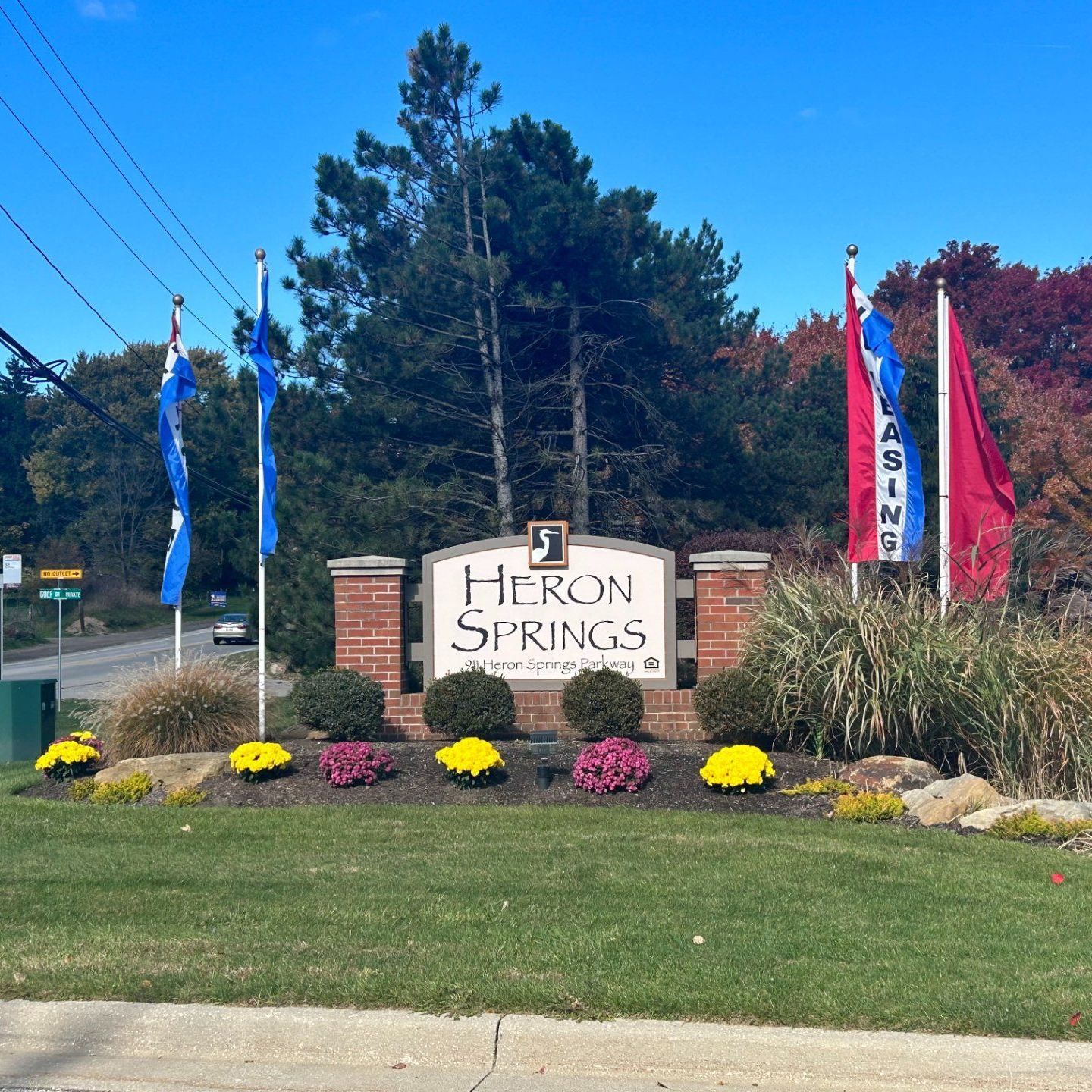 Sign for Heron Springs apartments with flags and colorful flowers.