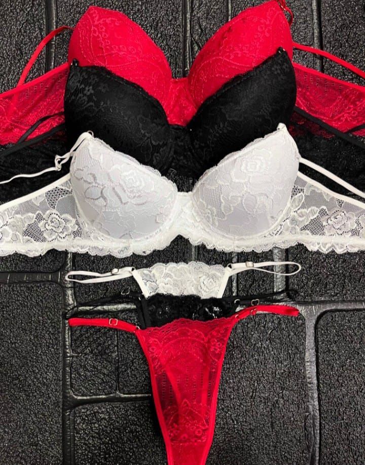 Mujer en lencería roja sentada en una cama, mirando hacia un lado.