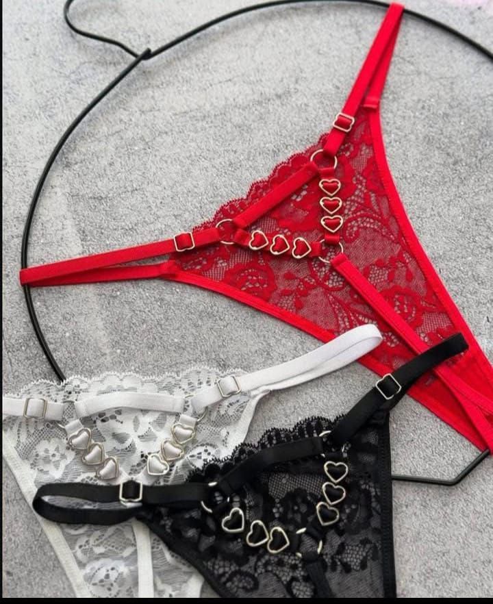Tres bragas de encaje tipo tanga: roja, blanca y negra, cada una con herrajes en forma de corazón.