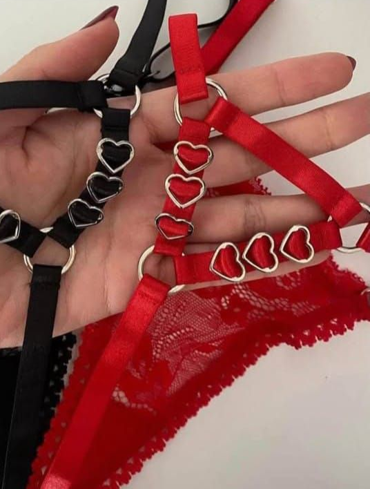 Primer plano de una mano sosteniendo lencería negra y roja con detalles en forma de corazón.