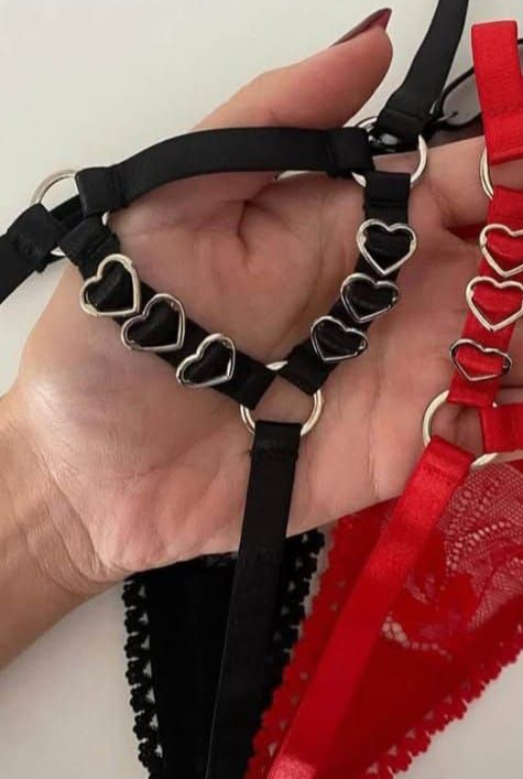 Mano sosteniendo lencería negra con detalles de corazones y una prenda de encaje rojo.