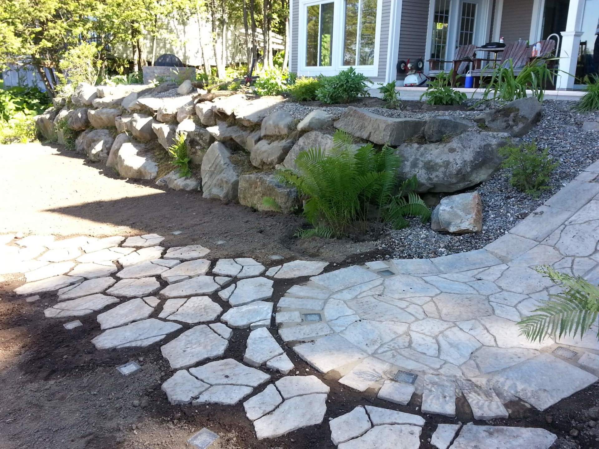 Une allée en pierre menant à une maison avec un grand mur de pierre en arrière-plan.