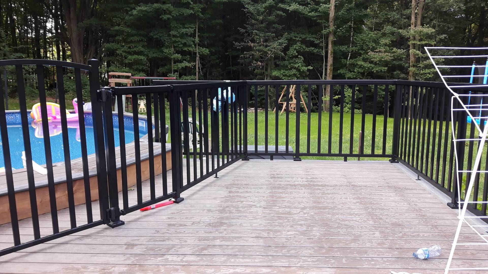 Une clôture entoure une terrasse en bois avec une piscine en arrière-plan