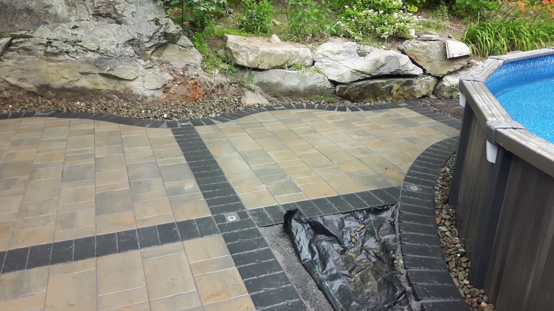Un patio avec une piscine en arrière-plan et un mur de pierre en arrière-plan.