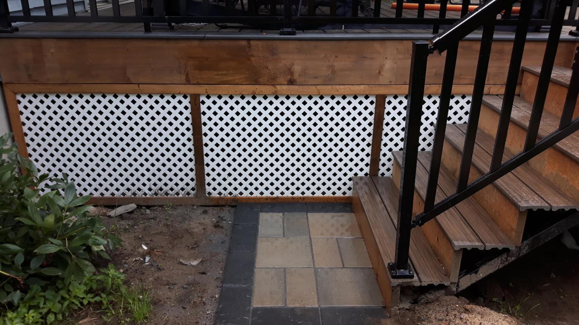 Une terrasse en bois avec des escaliers qui y mènent et une balustrade noire.