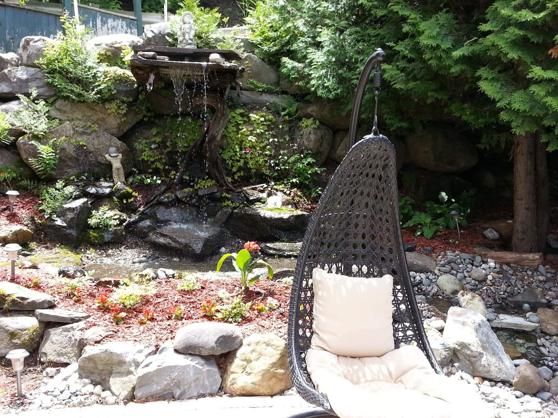 Une chaise suspendue dans un jardin avec une cascade en arrière-plan