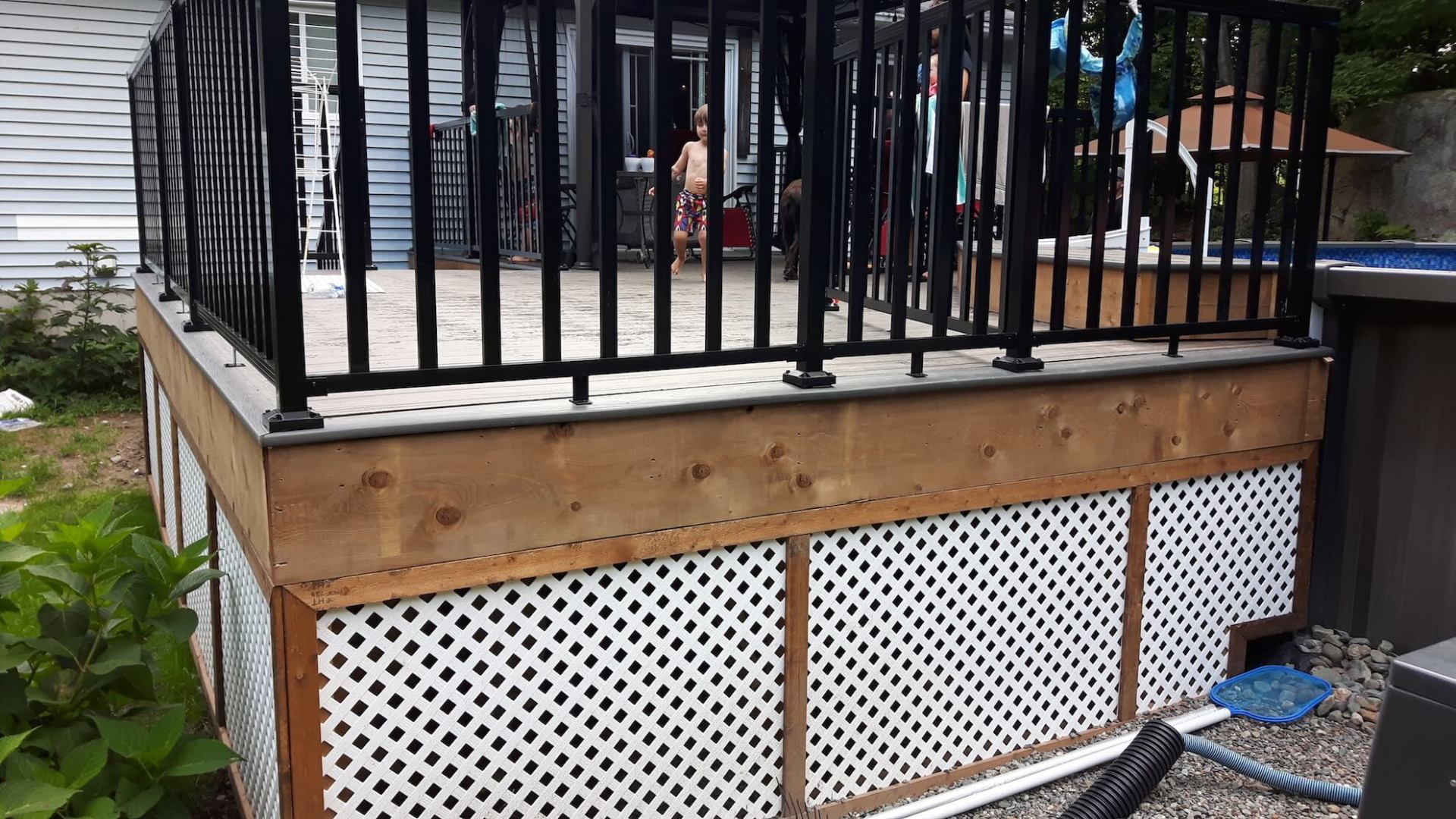 Une terrasse en bois avec une balustrade noire et un bain à remous en arrière-plan.