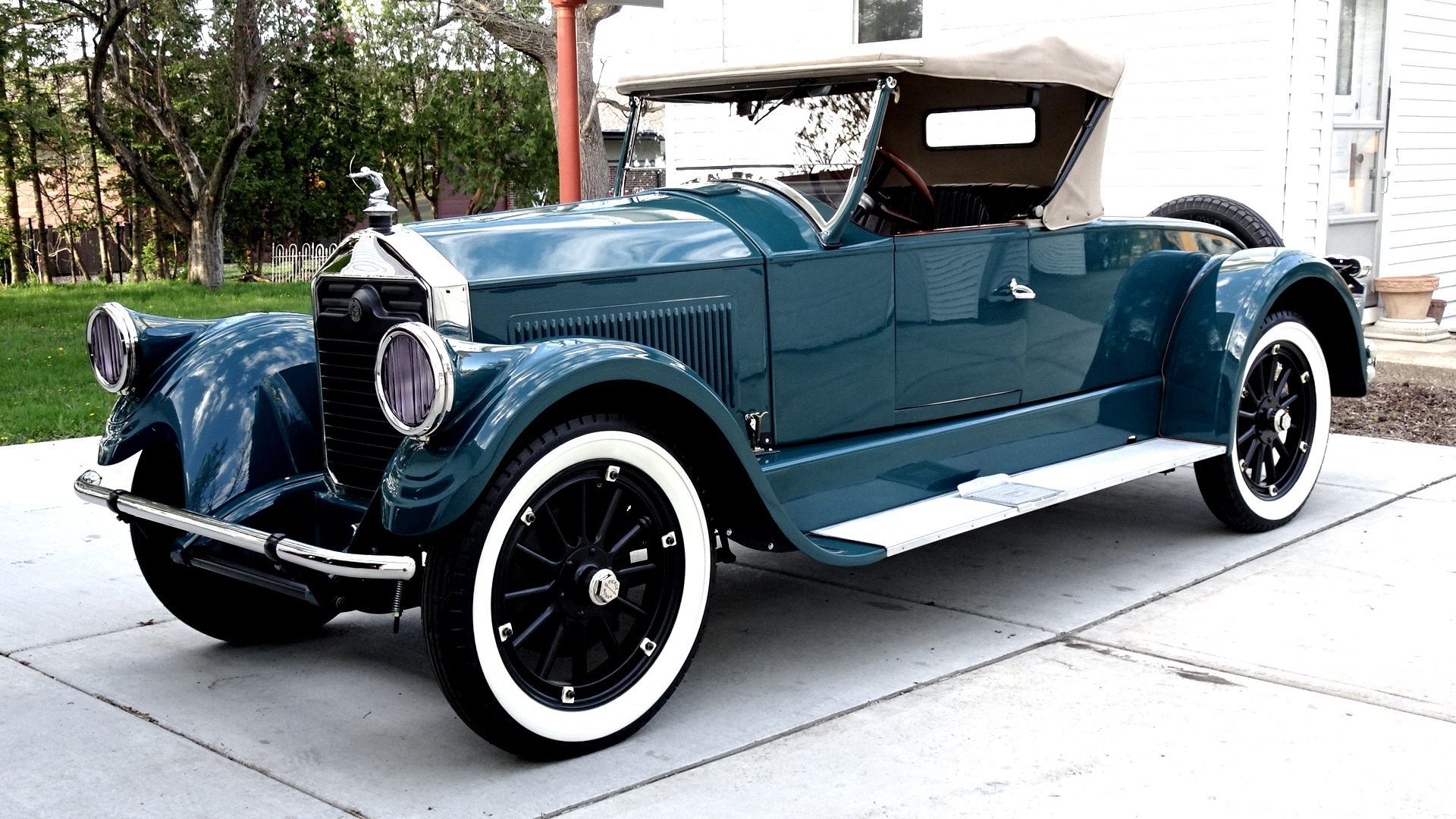 An old blue car with white tires is parked in a driveway.
