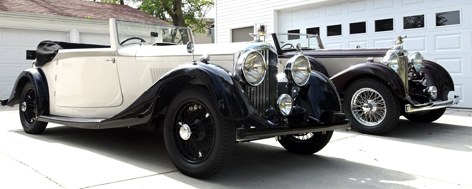 Two old cars are parked next to each other in front of a garage.