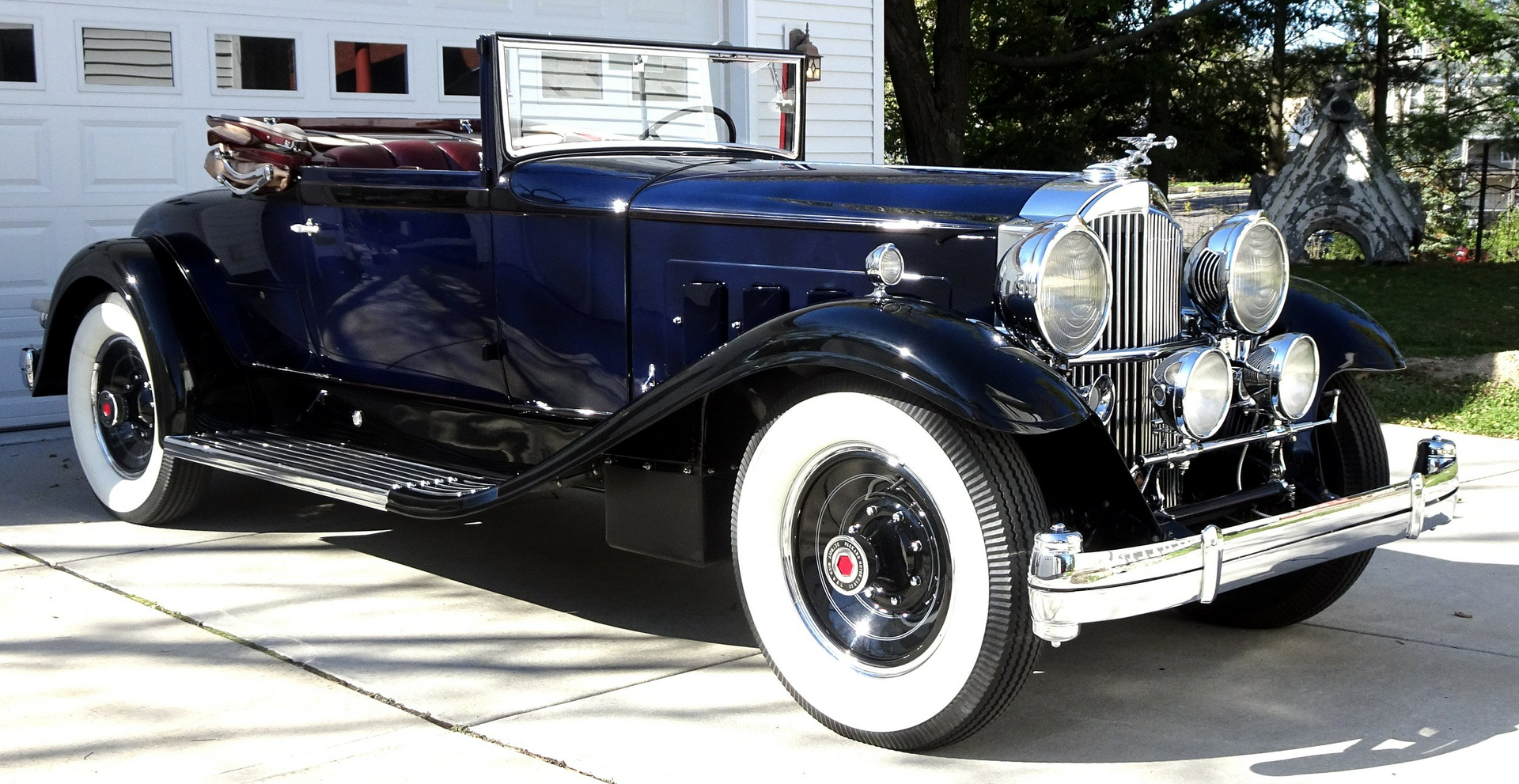 A blue car with white tires is parked in front of a garage