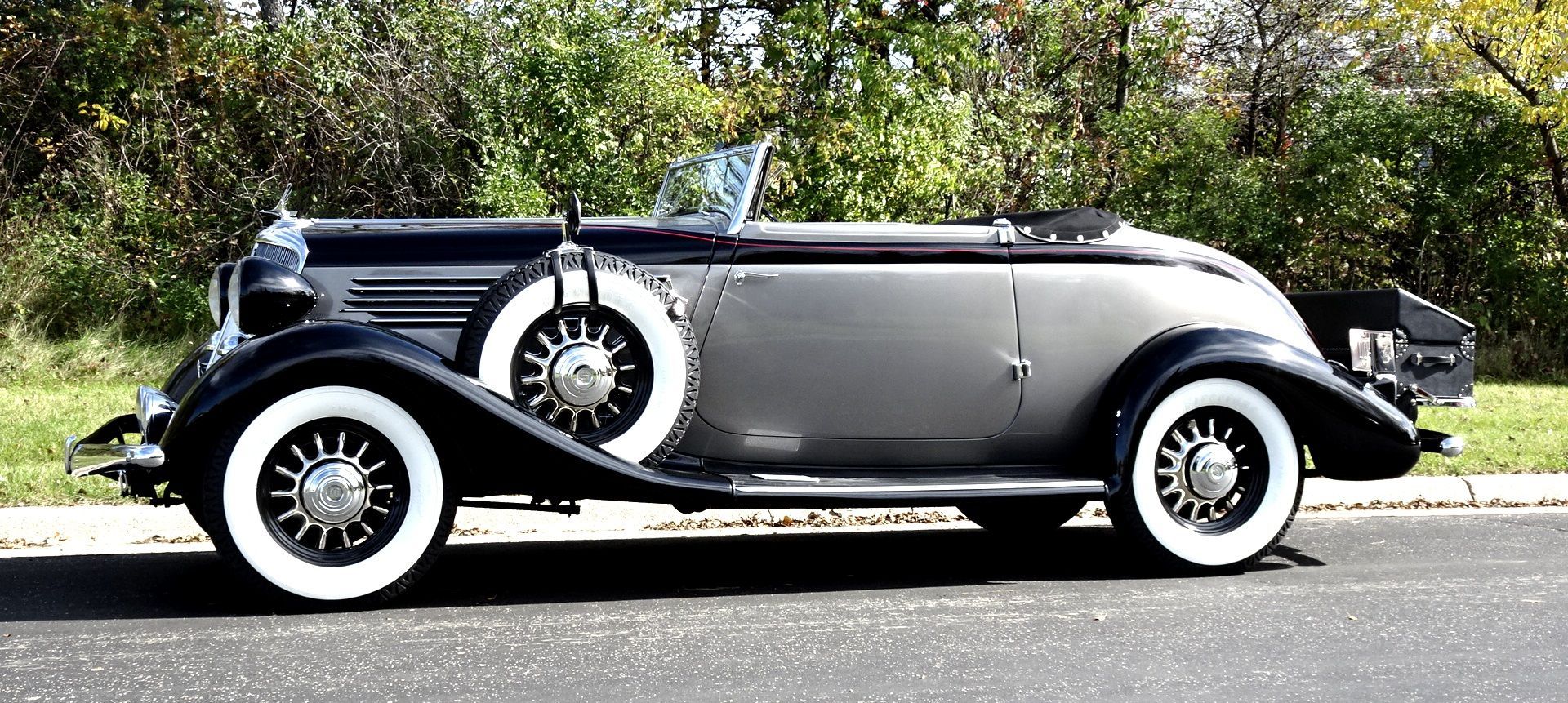 An old car with white tires is parked on the side of the road