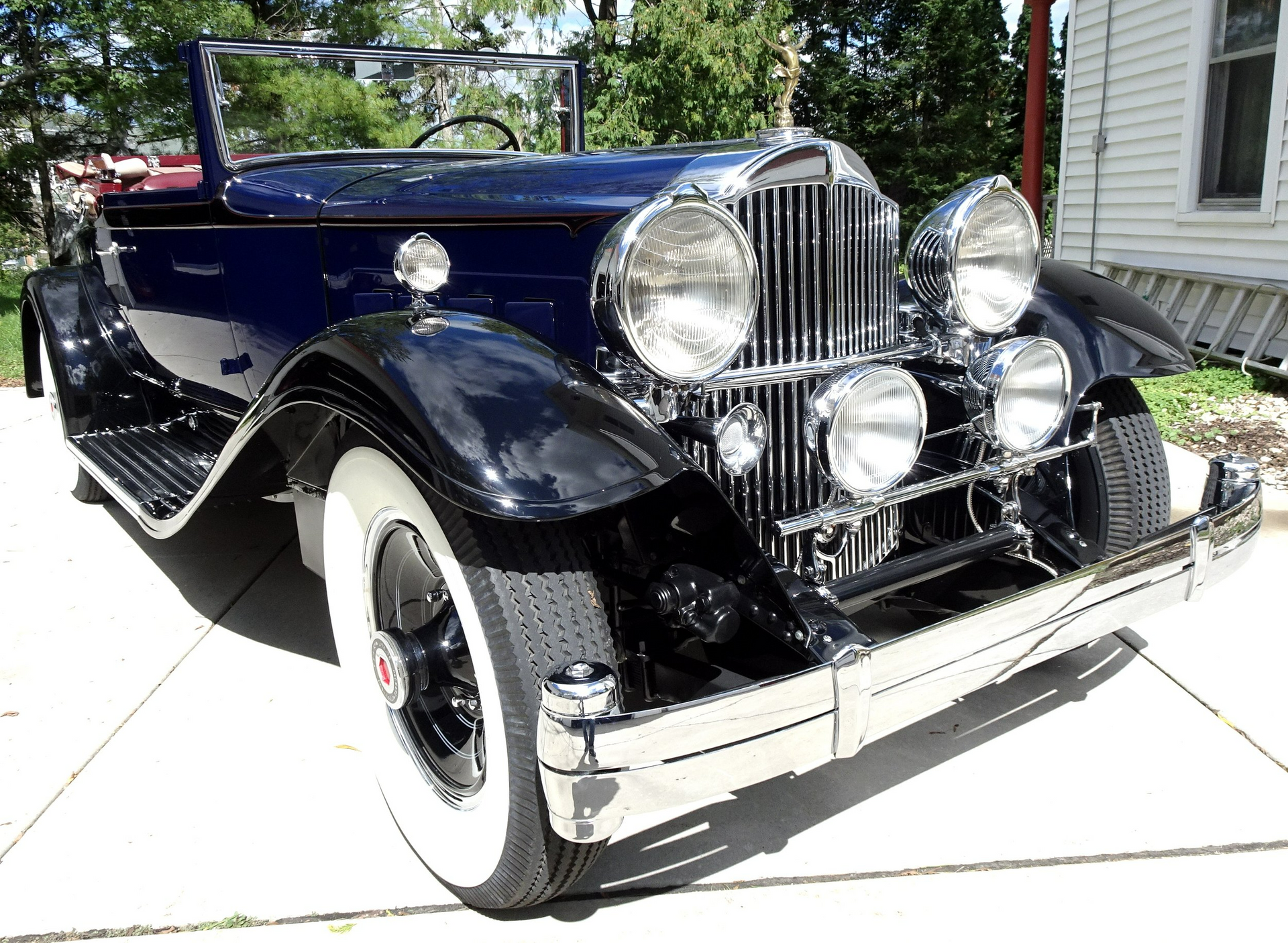 A black car with white tires is parked in front of a house