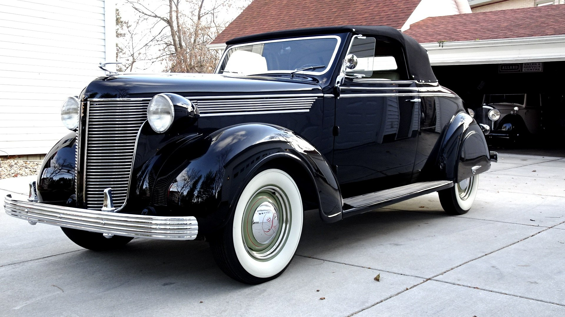 An old black car with white tires is parked in a driveway