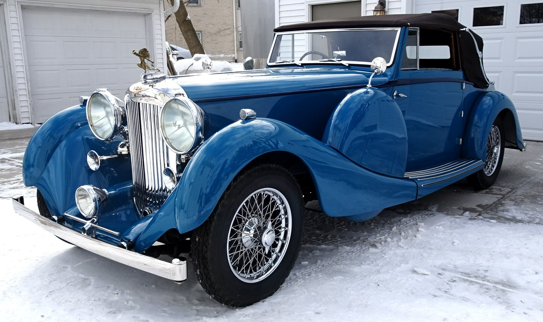 A blue car is parked in the snow in front of a garage.