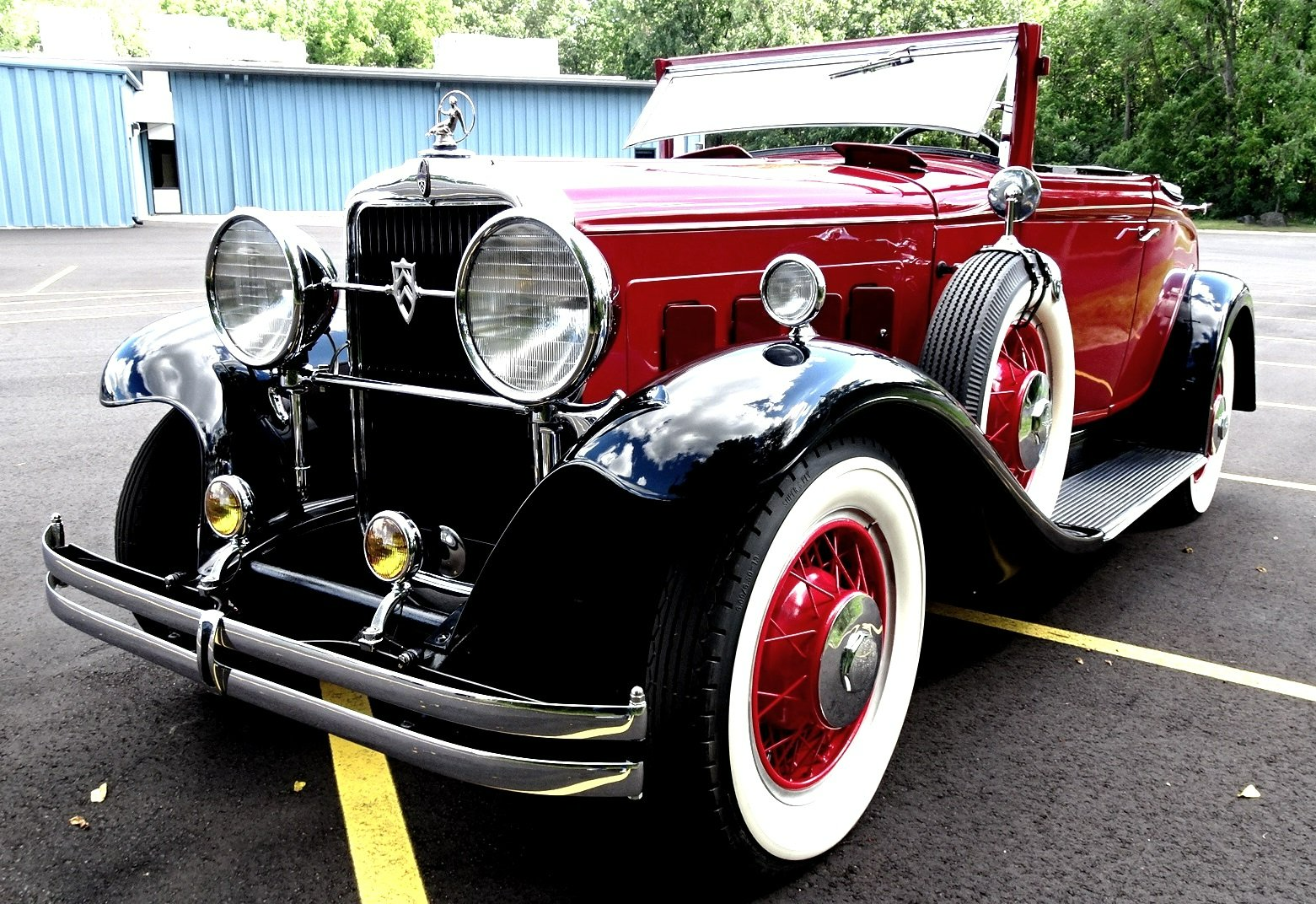 An old red car with white tires is parked in a parking lot