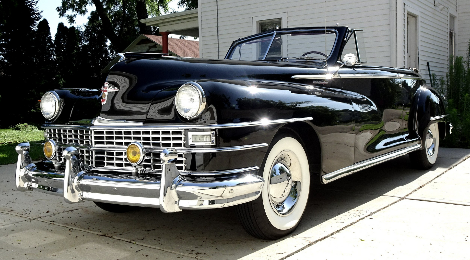 A black convertible is parked in front of a white house