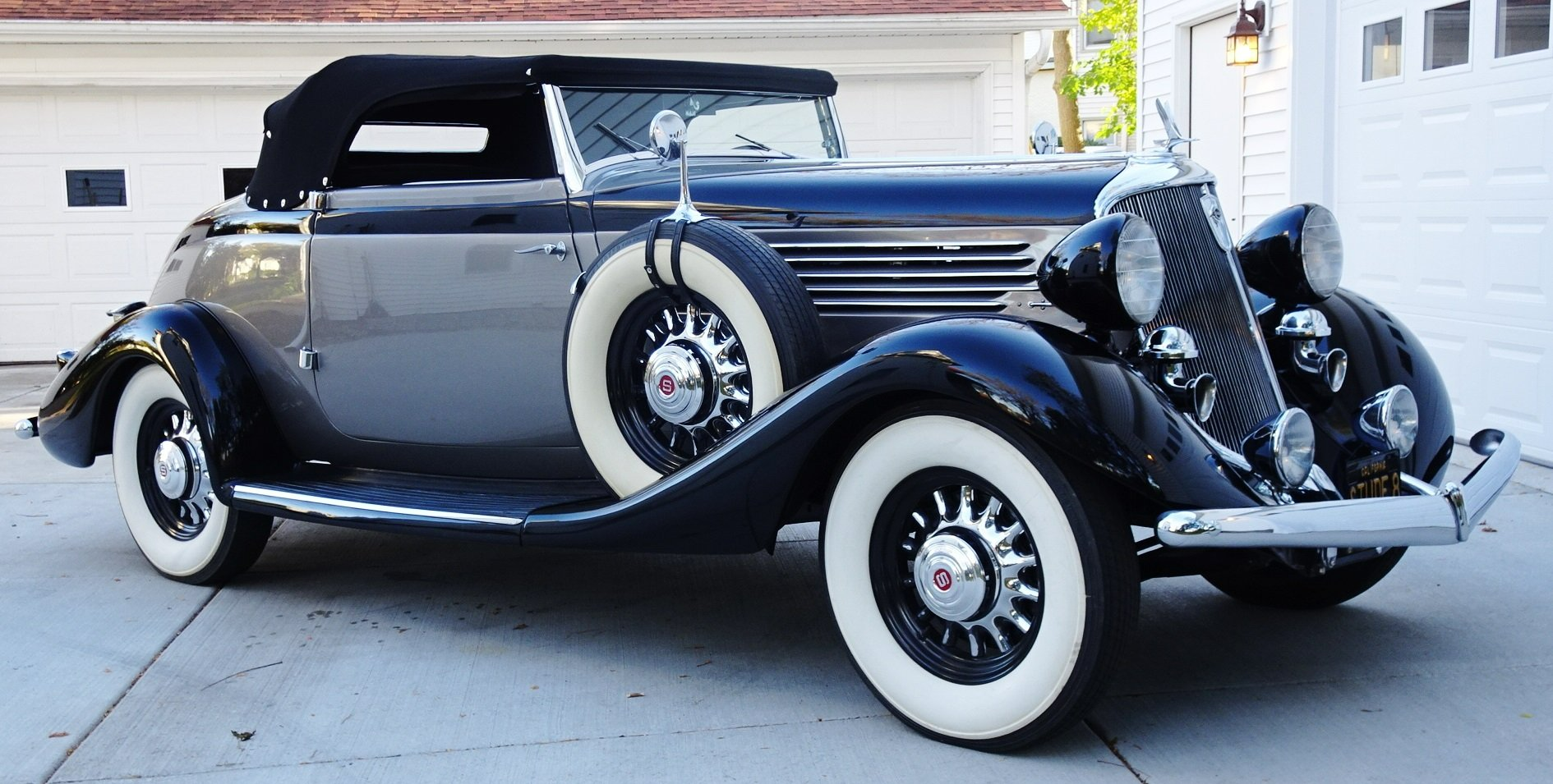A black car with white tires is parked in front of a garage
