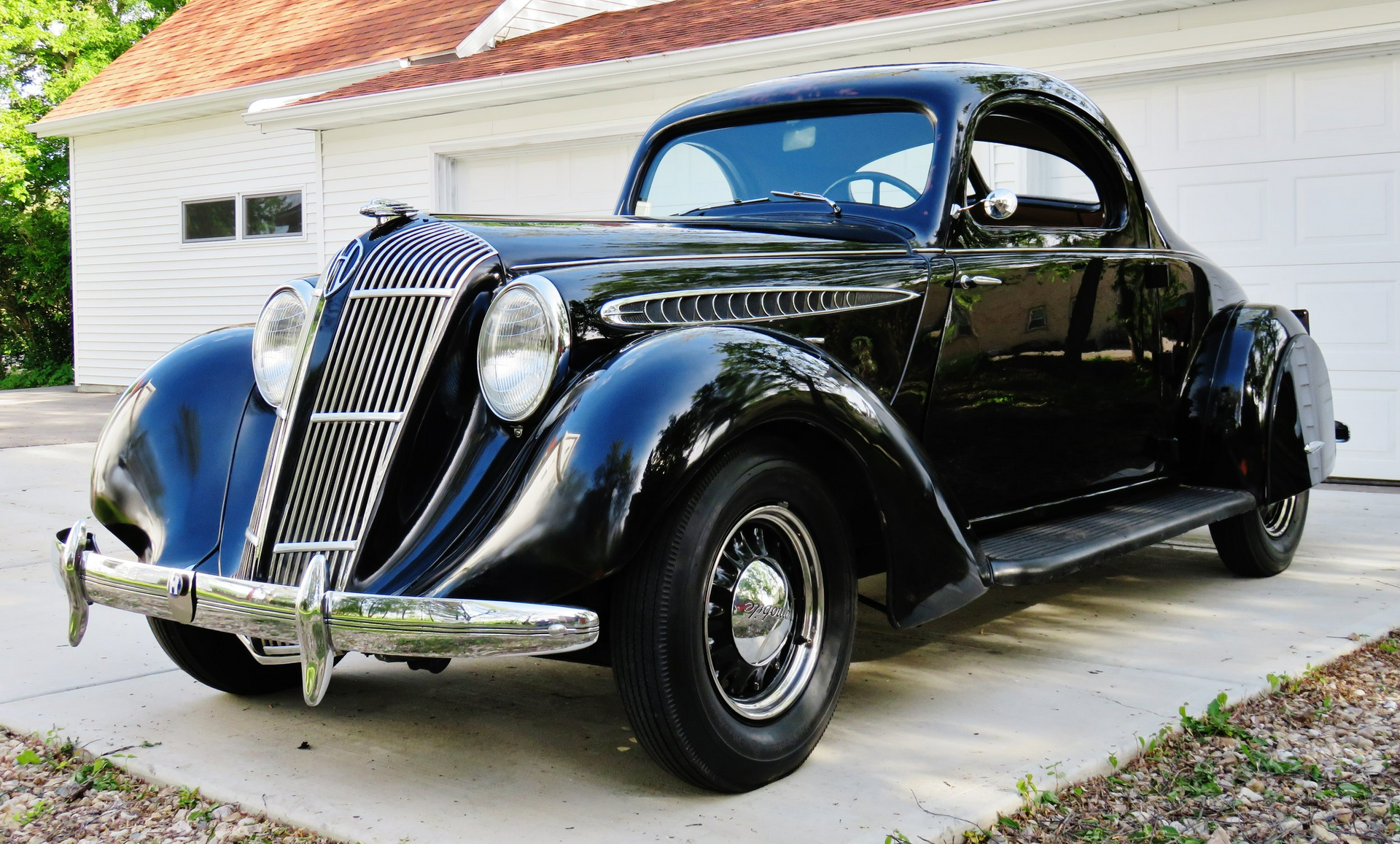An old black car is parked in front of a garage