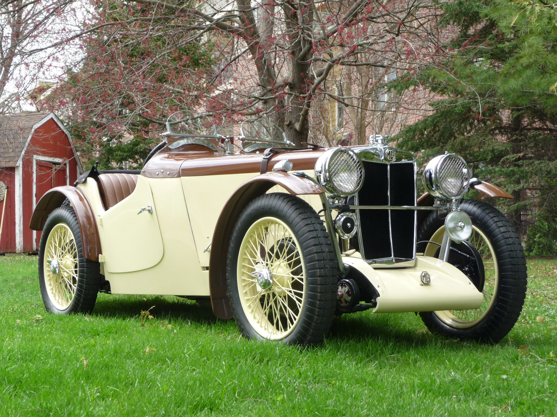 An old car is parked in the grass in front of a barn.